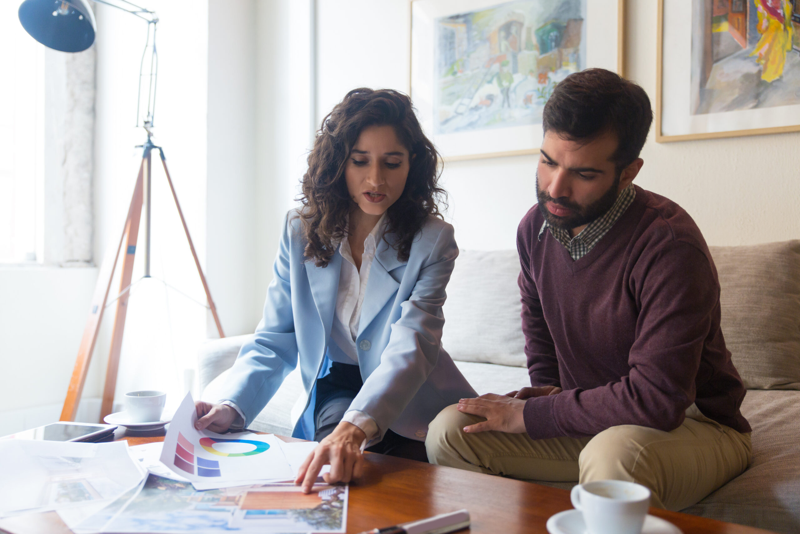 Focused design professional presenting renovation project to client. Young man and woman sitting in living room at home and talking. Working on renovation project concept